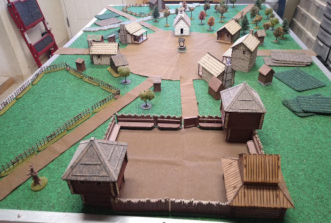 Tabletop miniature game setup with a vilage and many roads leading to it.